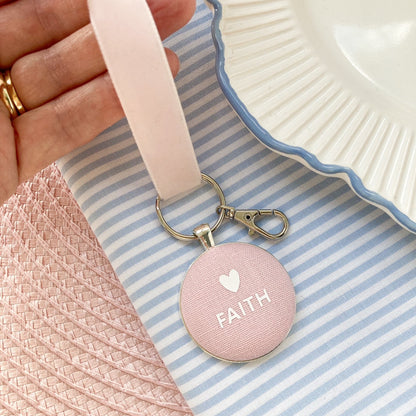 Pink keychain with 'FAITH' on a striped fabric background