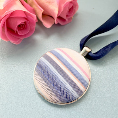 Memory fabric keepsake made with a striped shirt with a fabric message placed on a blue notebook with a pen and pink flowers.