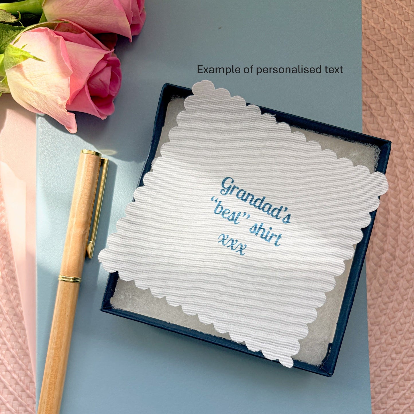 Memory fabric keepsake made with a striped shirt with a fabric message placed on a blue notebook with a pen and pink flowers.