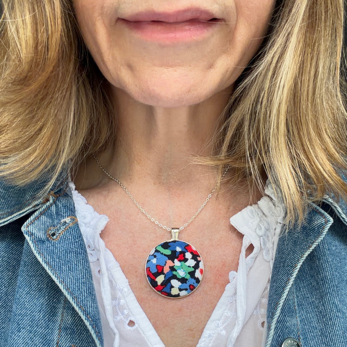 Person wearing a colorful pendant necklace with a denim jacket and white blouse.