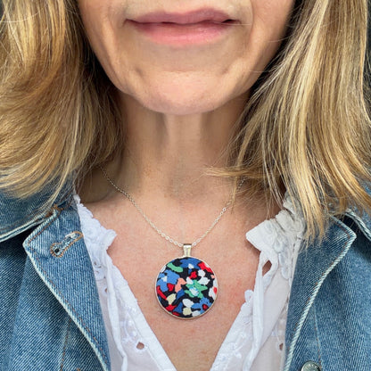 Person wearing a colorful pendant necklace with a denim jacket and white blouse.