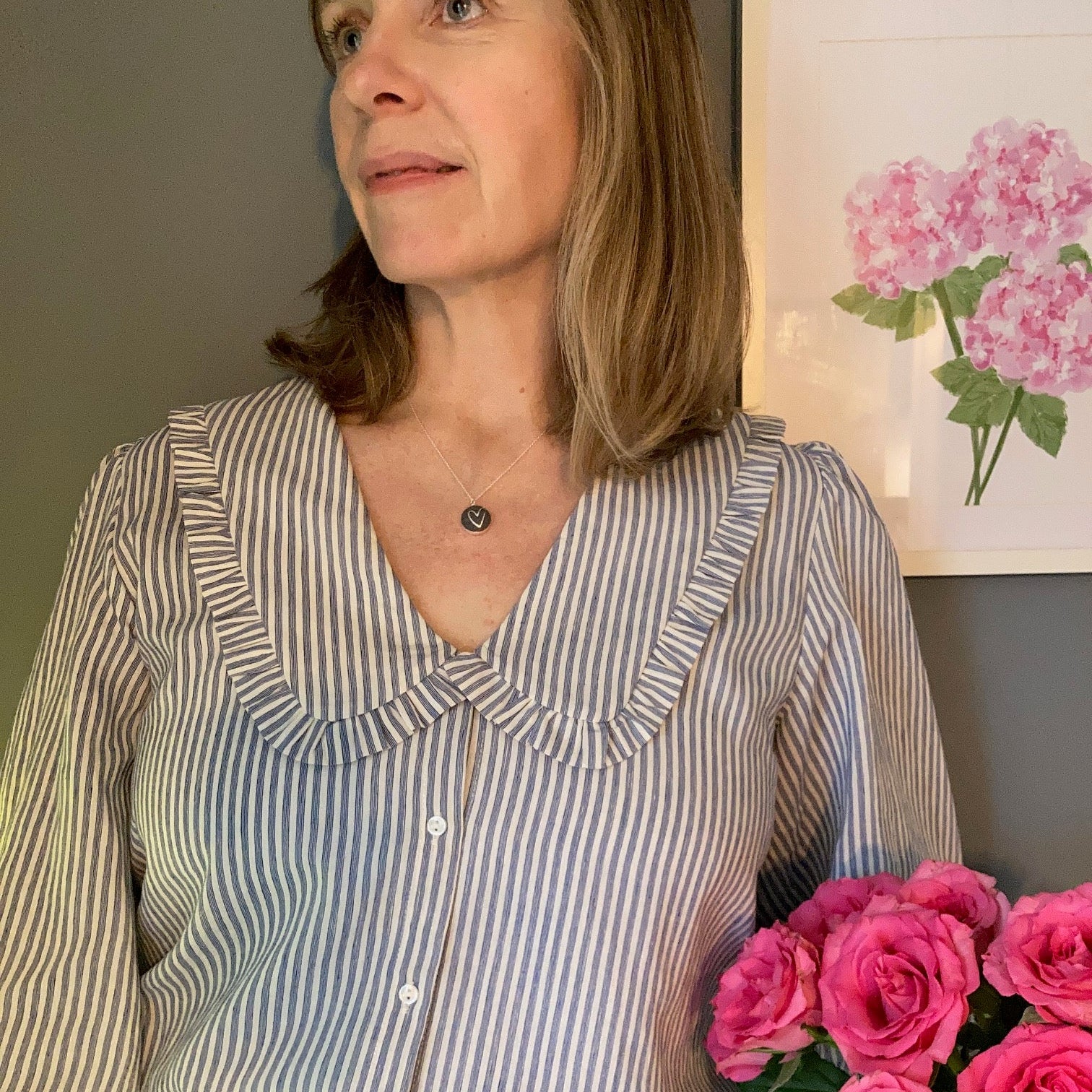 Woman wearing a dark grey necklace with heart design holding pink roses 
