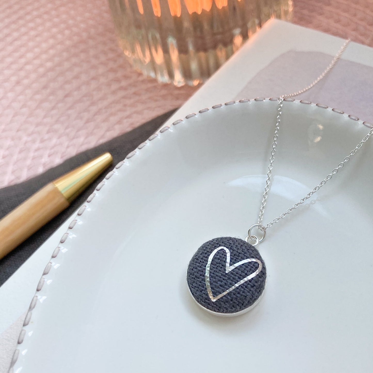 Necklace with a heart pendant on a white dish with a candle in the background