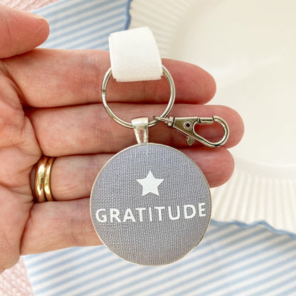 Keychain with 'GRATITUDE' and a star on a grey linen fabric