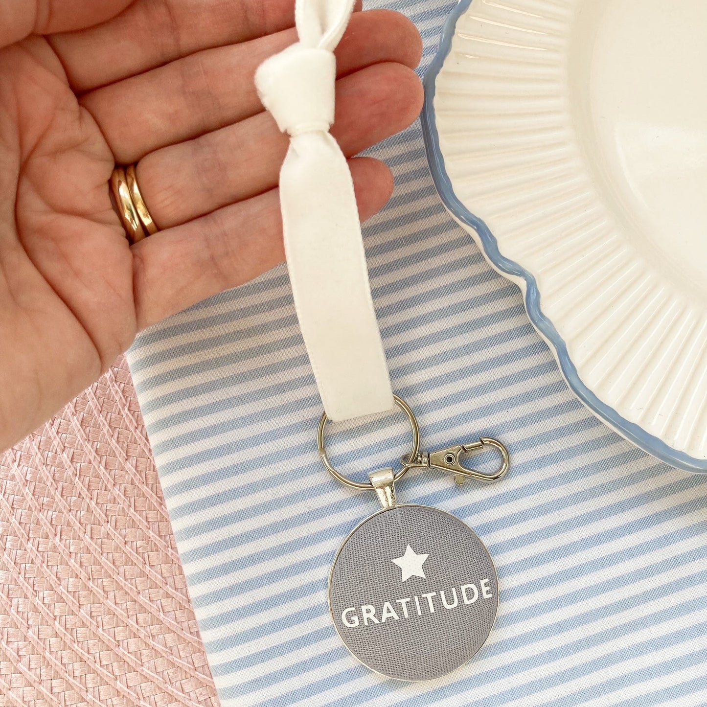Keyring and keepsake on a velvet ribbon with 'Gratitude' printed on grey fabric, held by a hand on a striped fabric background