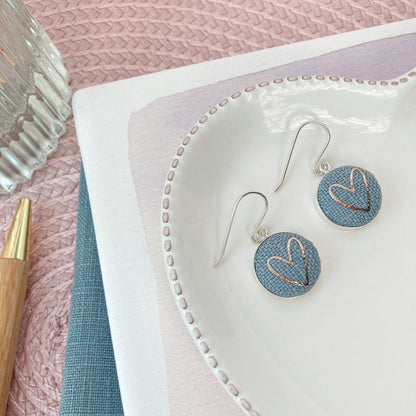 Pair of earrings on a white dish with a pink textured background