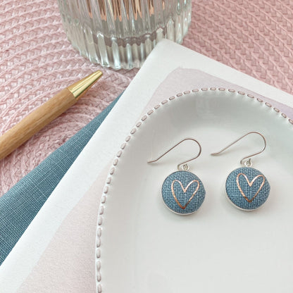 Pair of earrings with heart design on a white dish with a pink background
