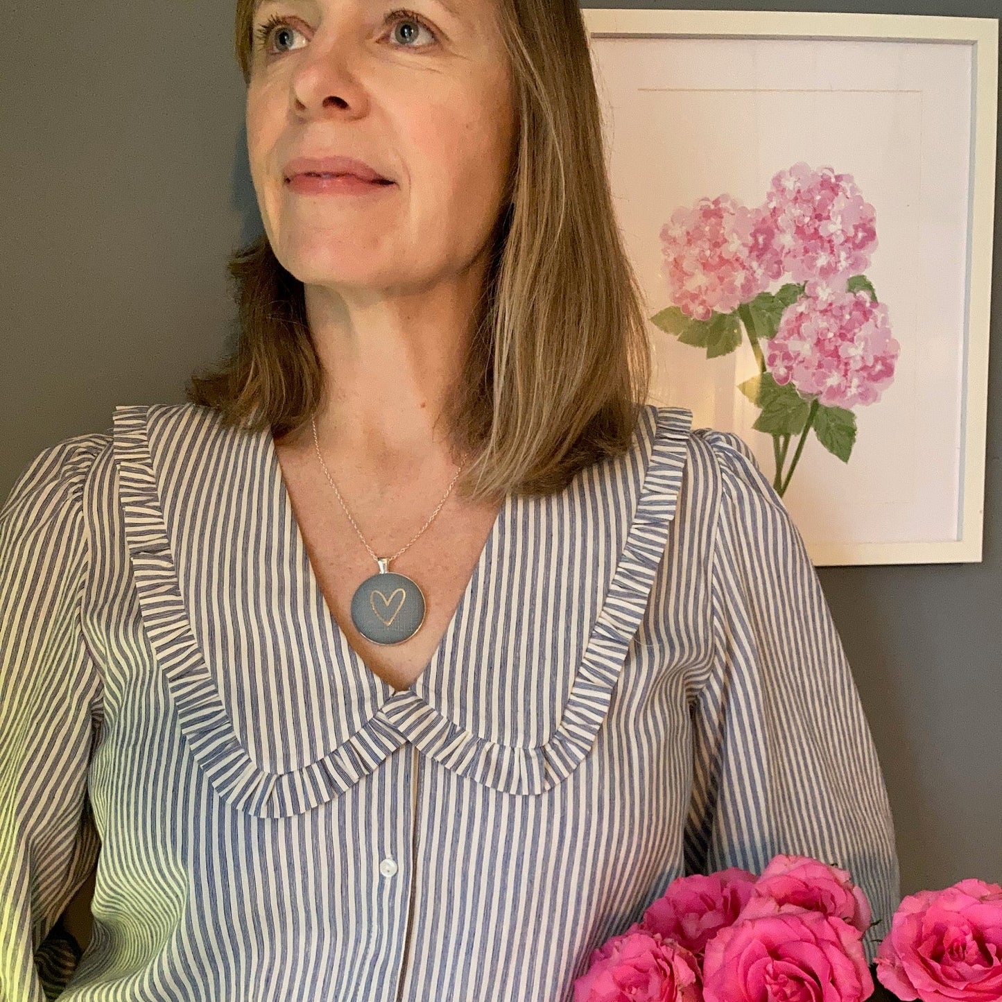 Person wearing a grey blue pendant and striped shirt with pink flowers in the background