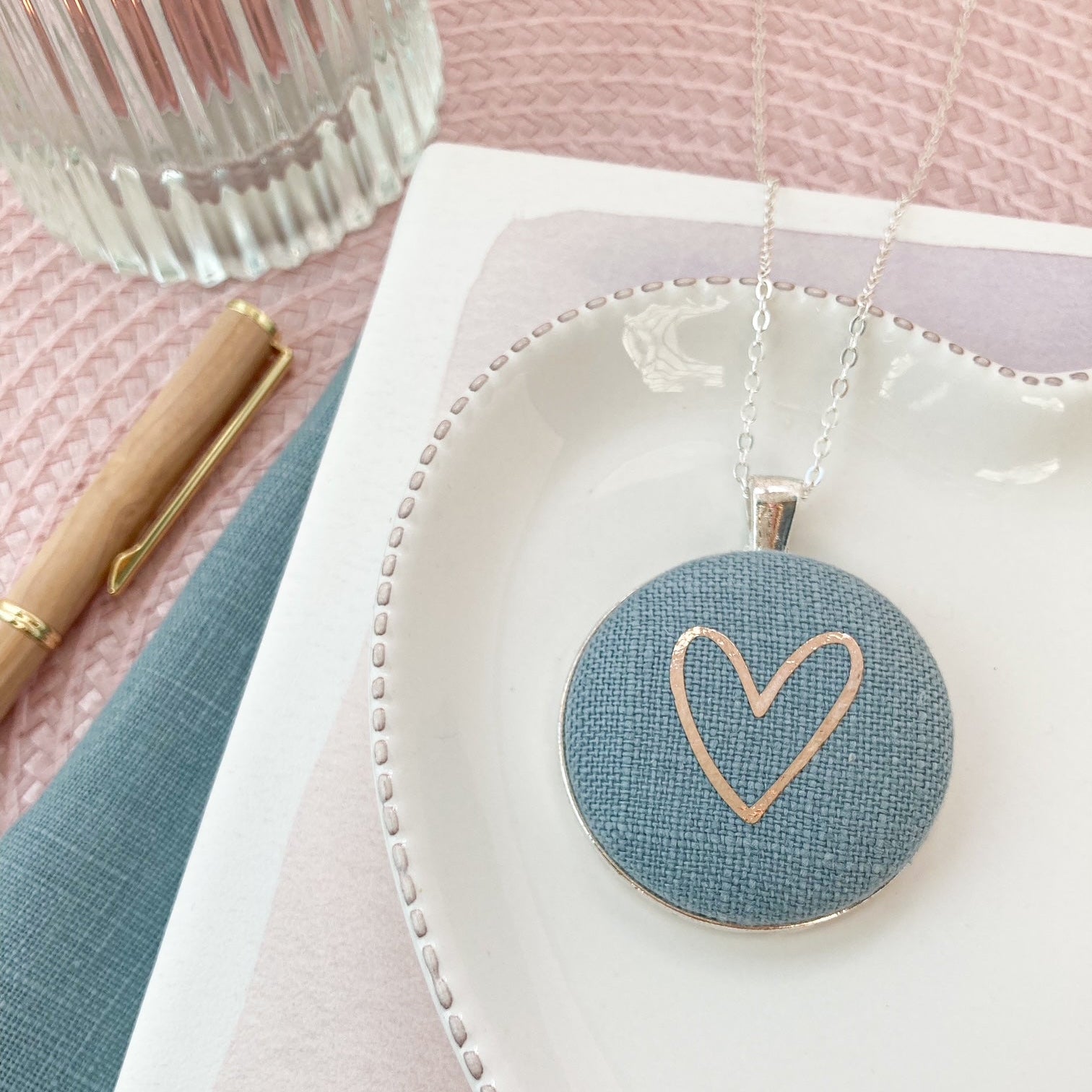 Necklace with a heart pendant on a white dish with a pink background