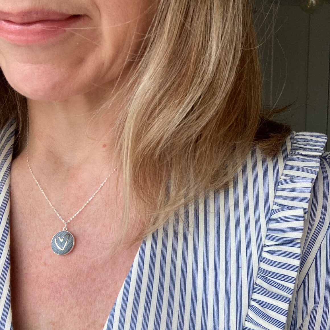 Woman wearing a grey blue necklace with heart design and striped shirt