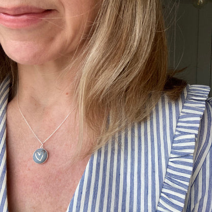 Woman wearing a grey blue necklace with heart design and striped shirt
