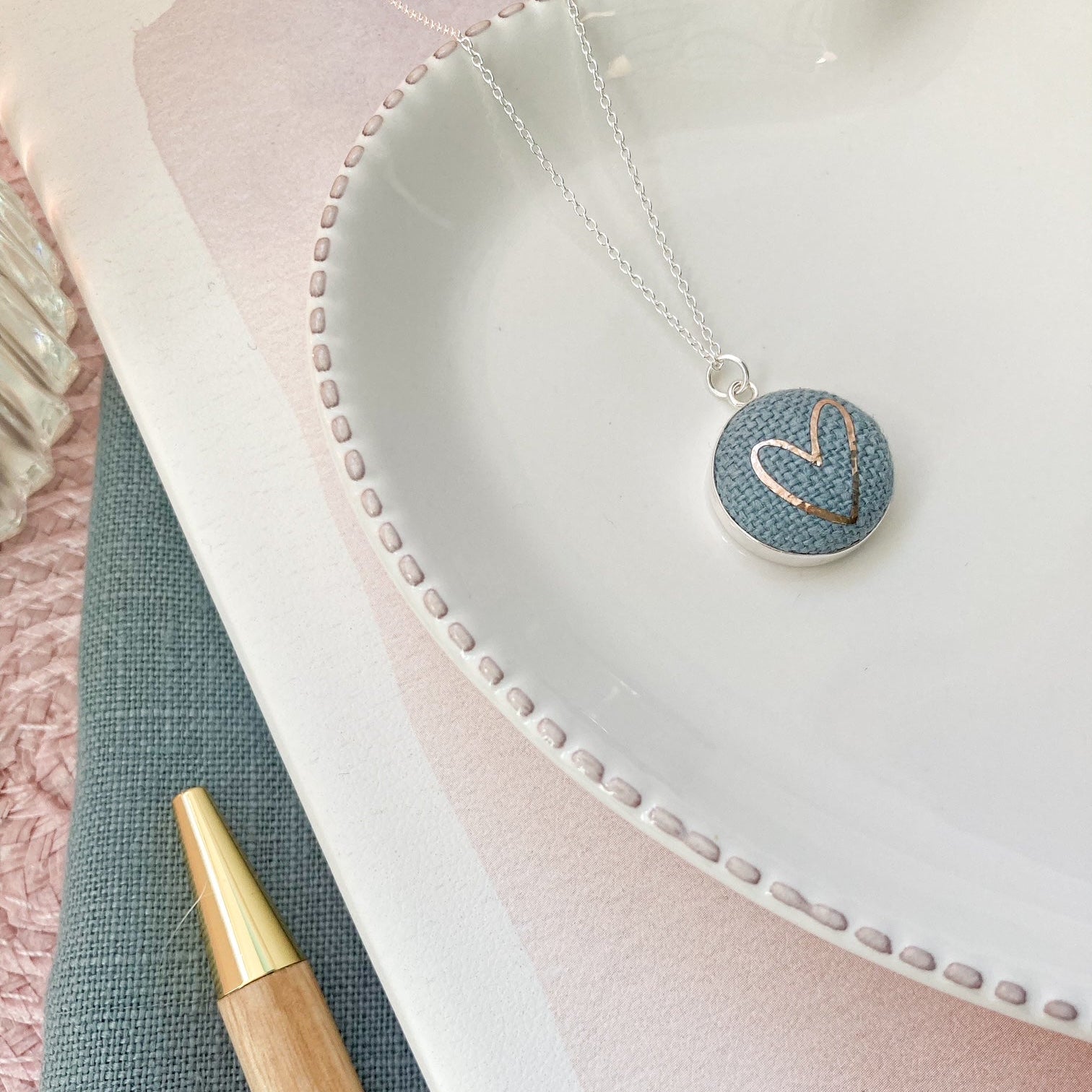 Necklace with a heart-shaped pendant on a textured surface with a pen.