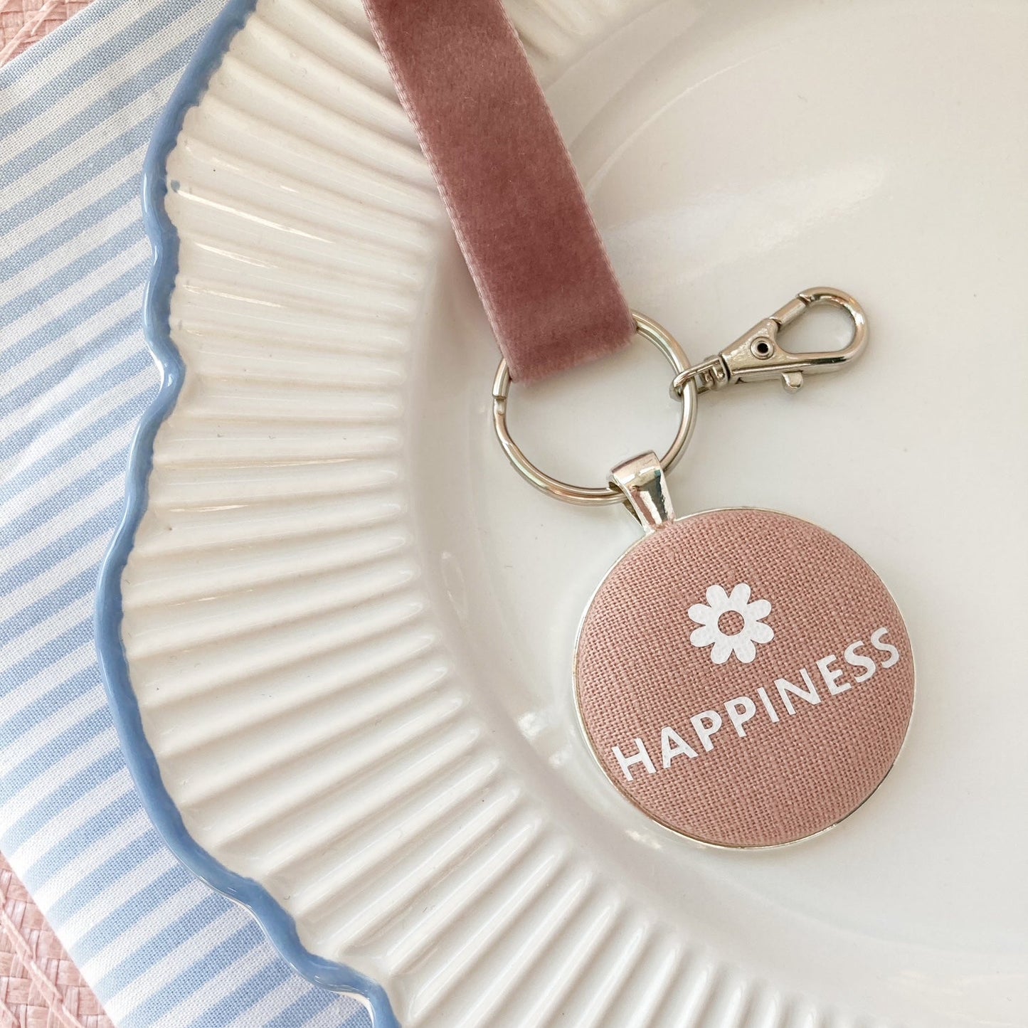 Keychain with 'Happiness' and a flower printed on pink blush fabric, on a decorative plate