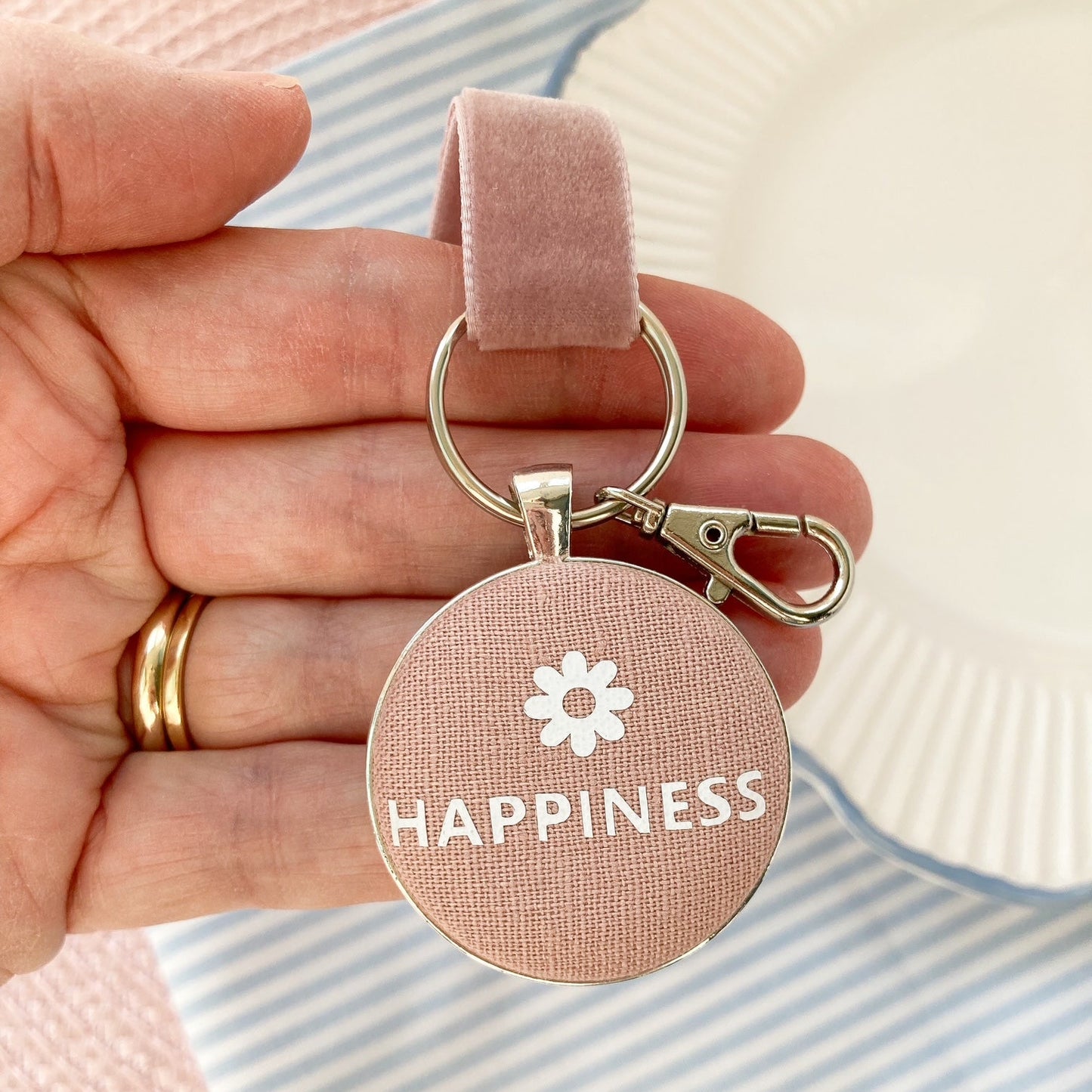 Keyring and keepsake with 'Happiness' and a flower symbol held by a hand on a striped background