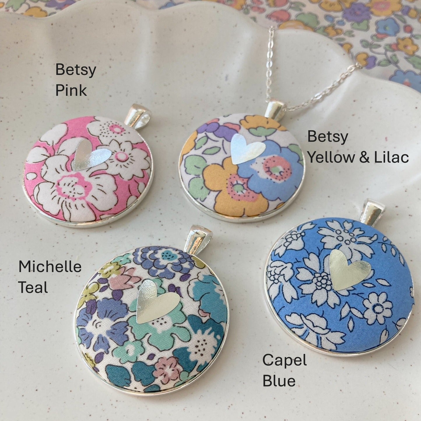 Four floral pendant necklaces with labels on a patterned background