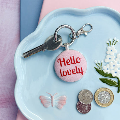 Keyring with 'Hello lovely' charm on a blue dish with coins and flowers
