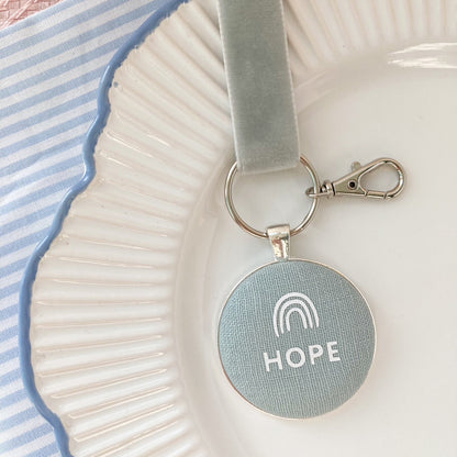 Keychain with 'HOPE' and rainbow symbol on a duck egg blue fabric