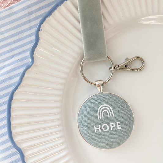 Keychain with 'HOPE' and rainbow symbol on a duck egg blue fabric