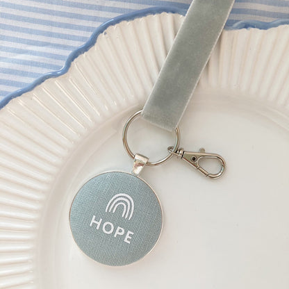 Key ring and keepsake with 'HOPE' and a rainbow design, laid on a plate with striped fabric background