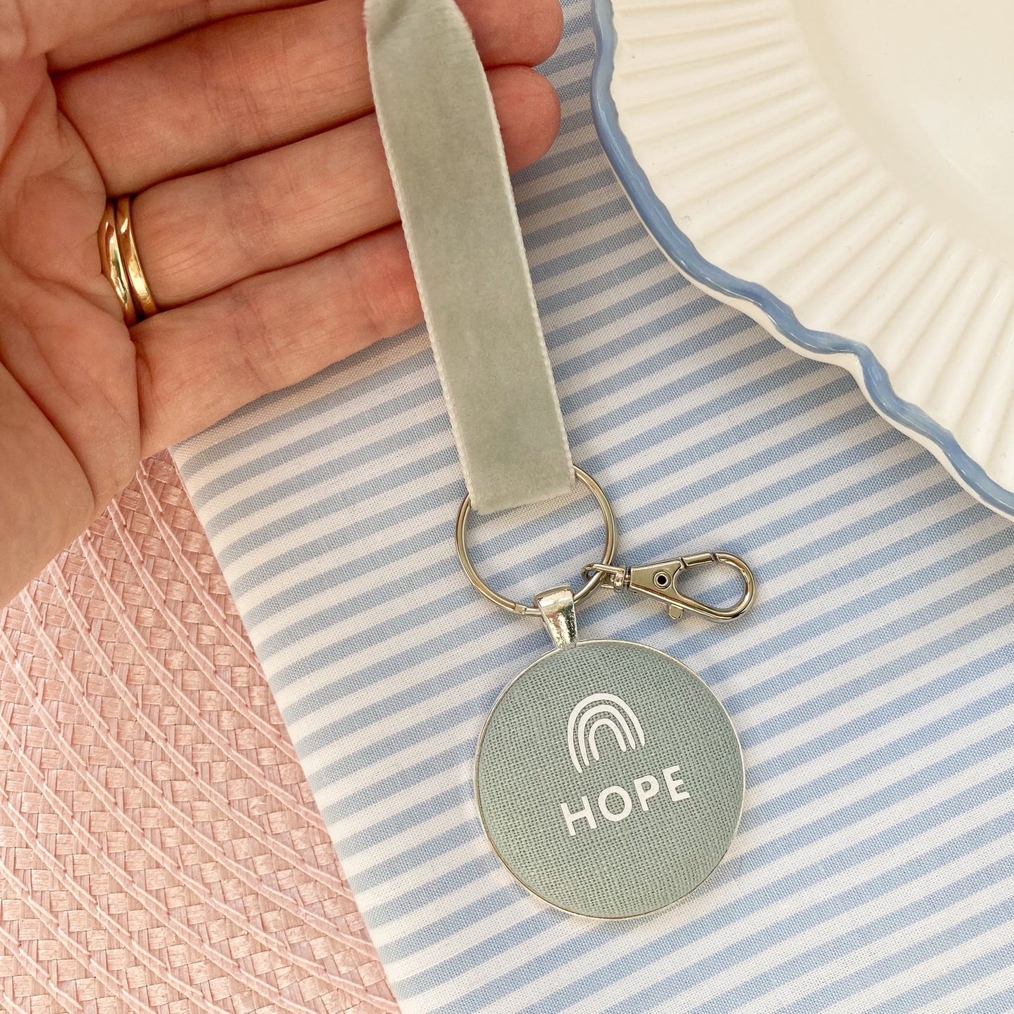 Keychain with 'HOPE' and a rainbow printed onto fabric, held over a striped fabric background