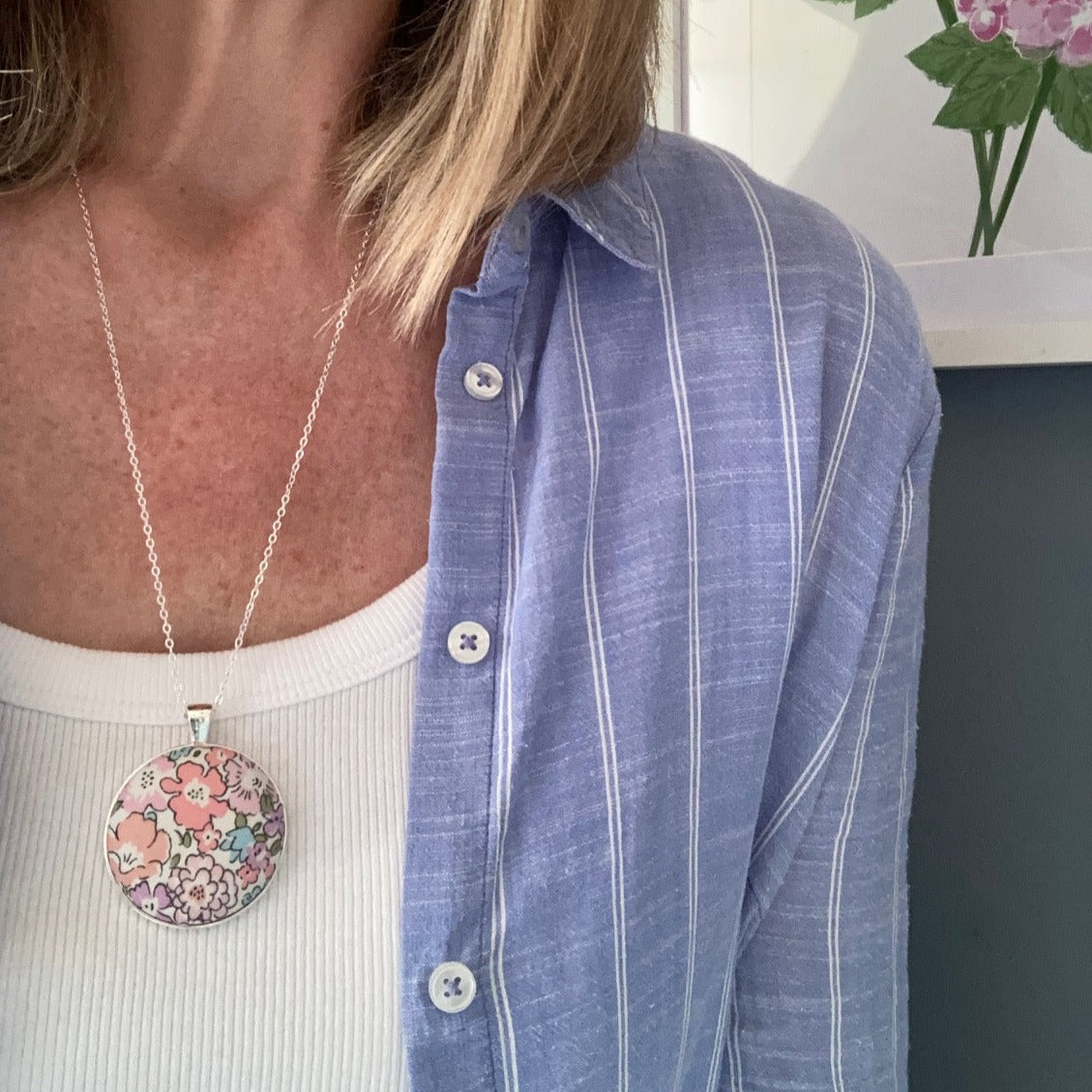 Woman wearing a pink floral fabric necklace with a white vest and blue shirt