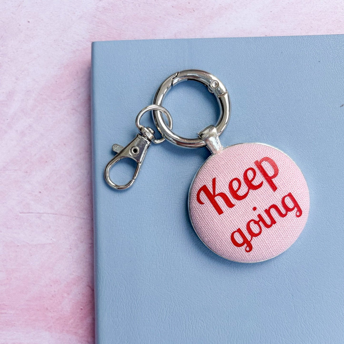 Pink keyring with 'Keep going' text printed onto pink fabric, on a light blue background