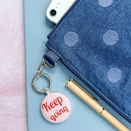 Blue polka dot pouch with a phone, pen, and 'Keep going' keychain on a light pink background