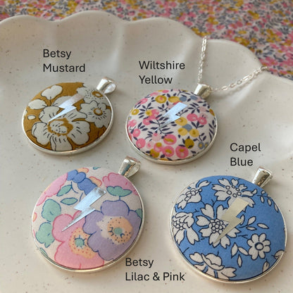 Four floral pendant necklaces on a white dish with a colorful patterned background.