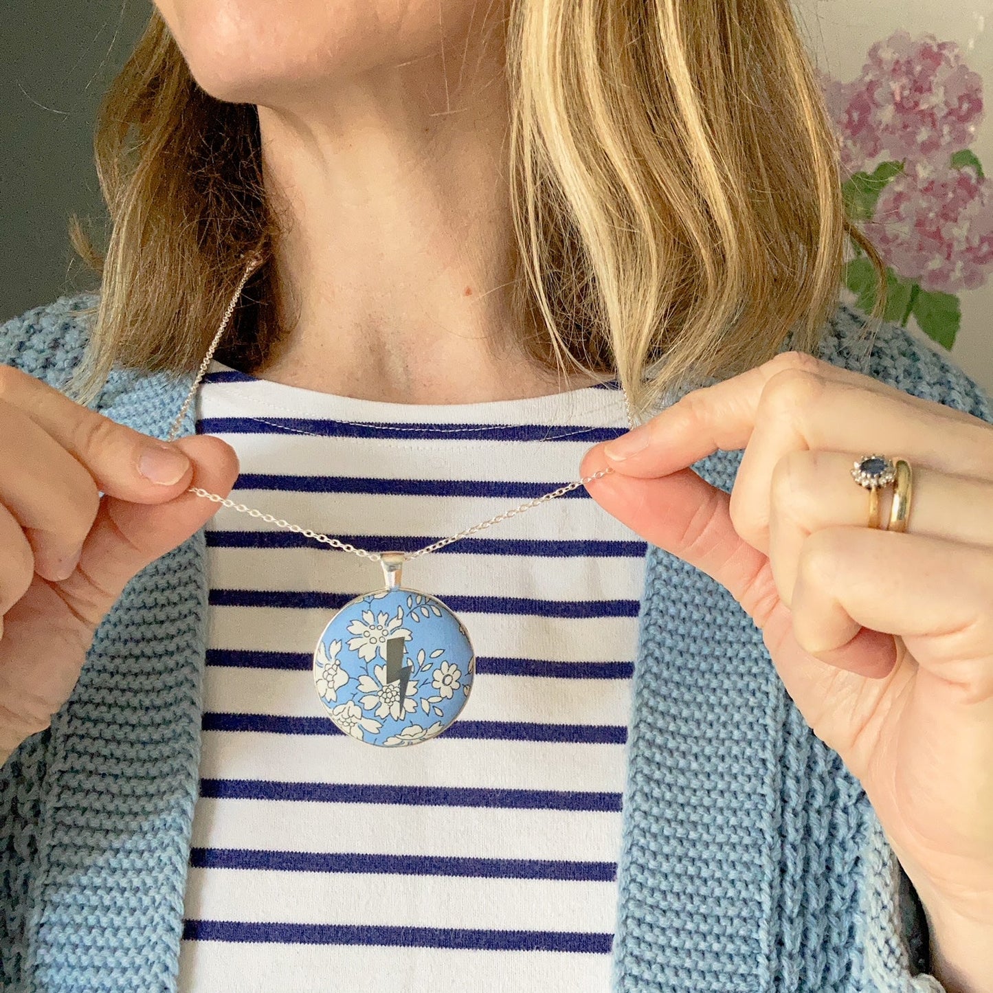 Person wearing a blue and white striped top with a necklace featuring a lightning and blue floral pendant