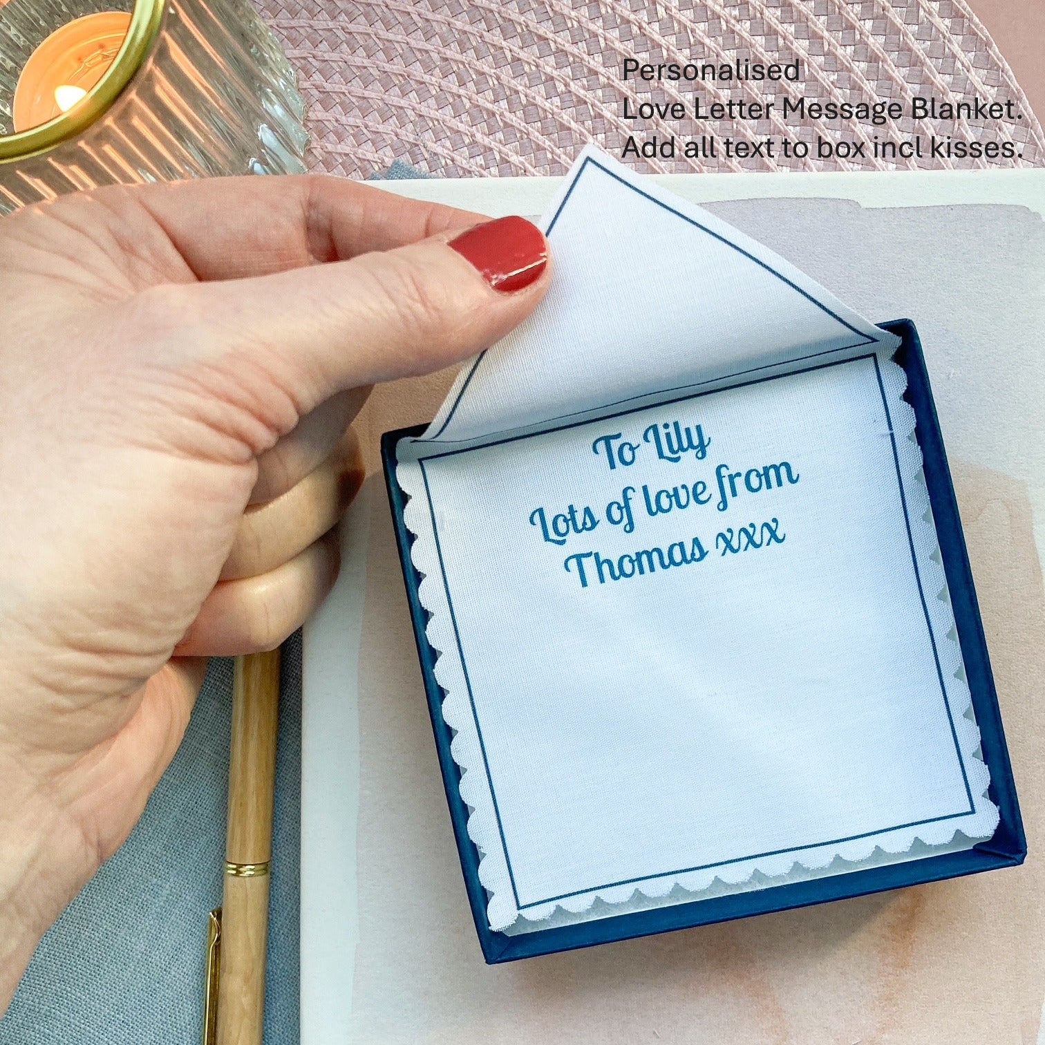 Personalised love letter message blanket with a hand holding it and a pen on a textured surface.