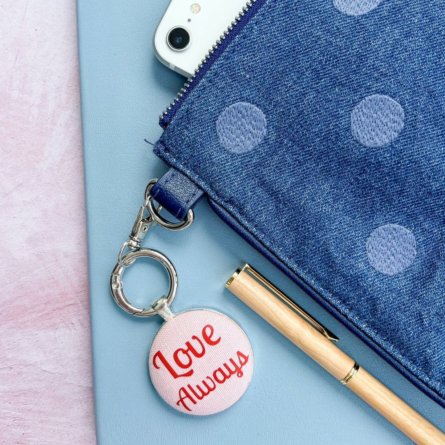 Blue polka dot pouch with a 'Love Always' charm keyring on a light pink background
