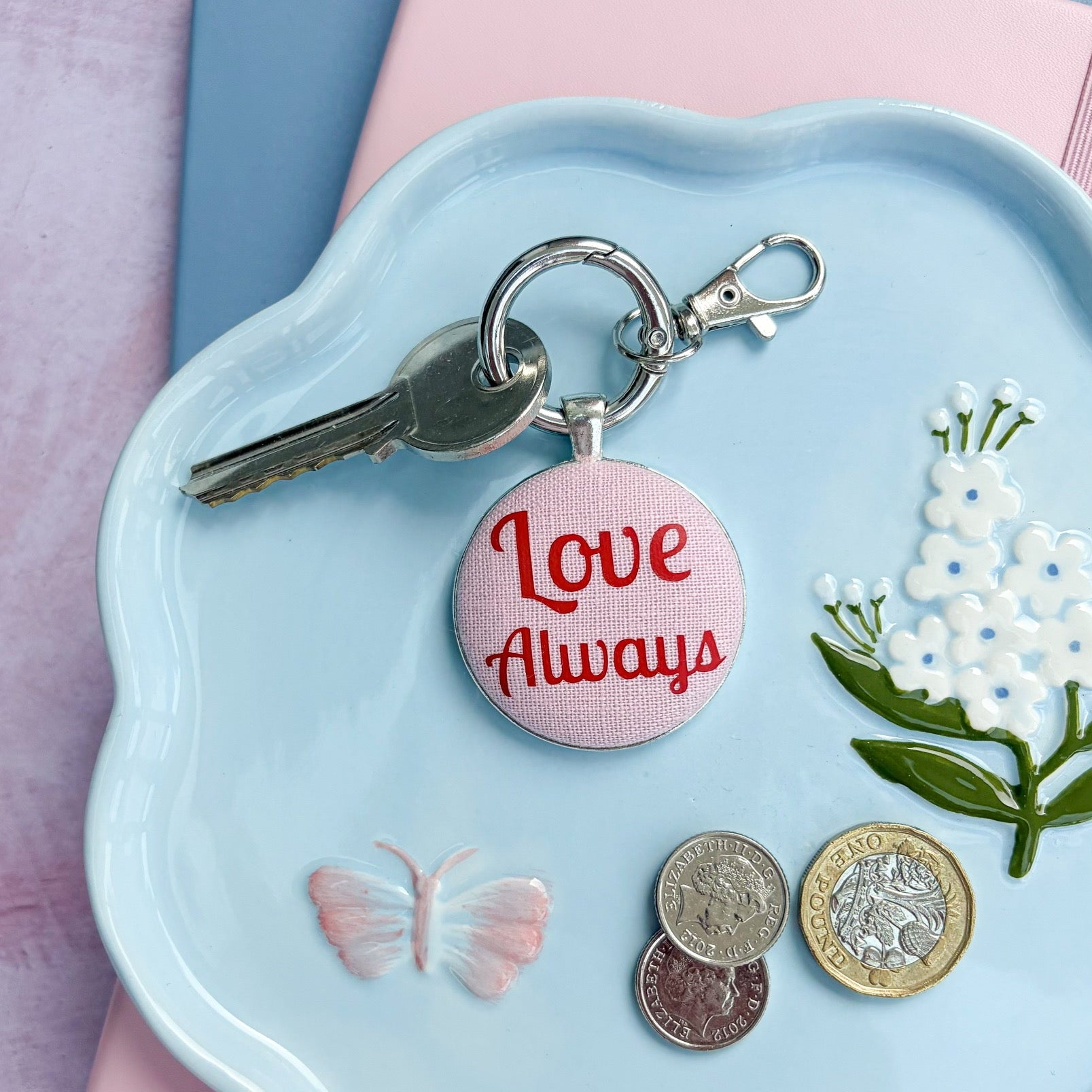 Pink and red keyring with 'Love Always' words, set on a decorative plate with coins and flowers