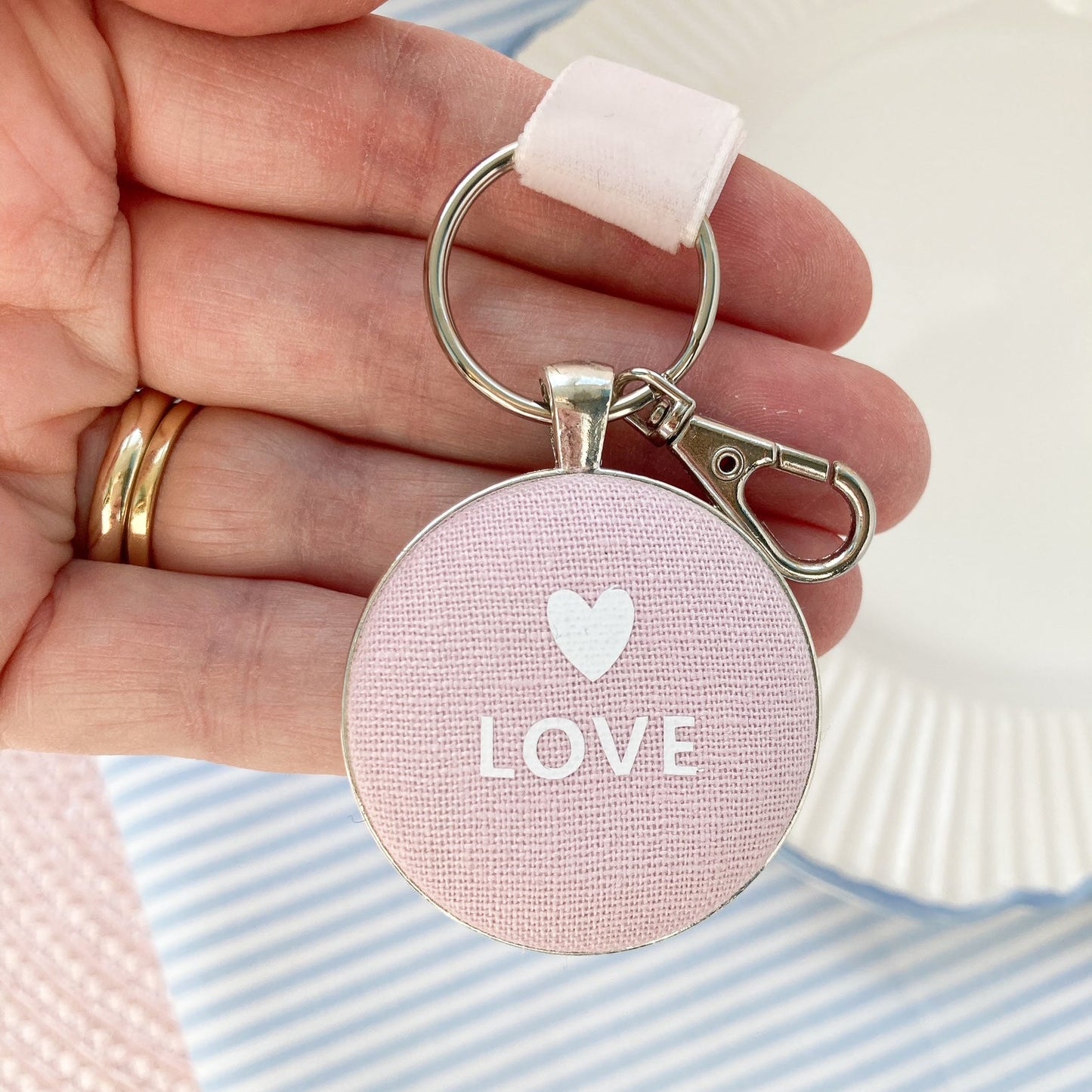Pink keyring with 'LOVE' and heart design held in a hand against a striped fabric background