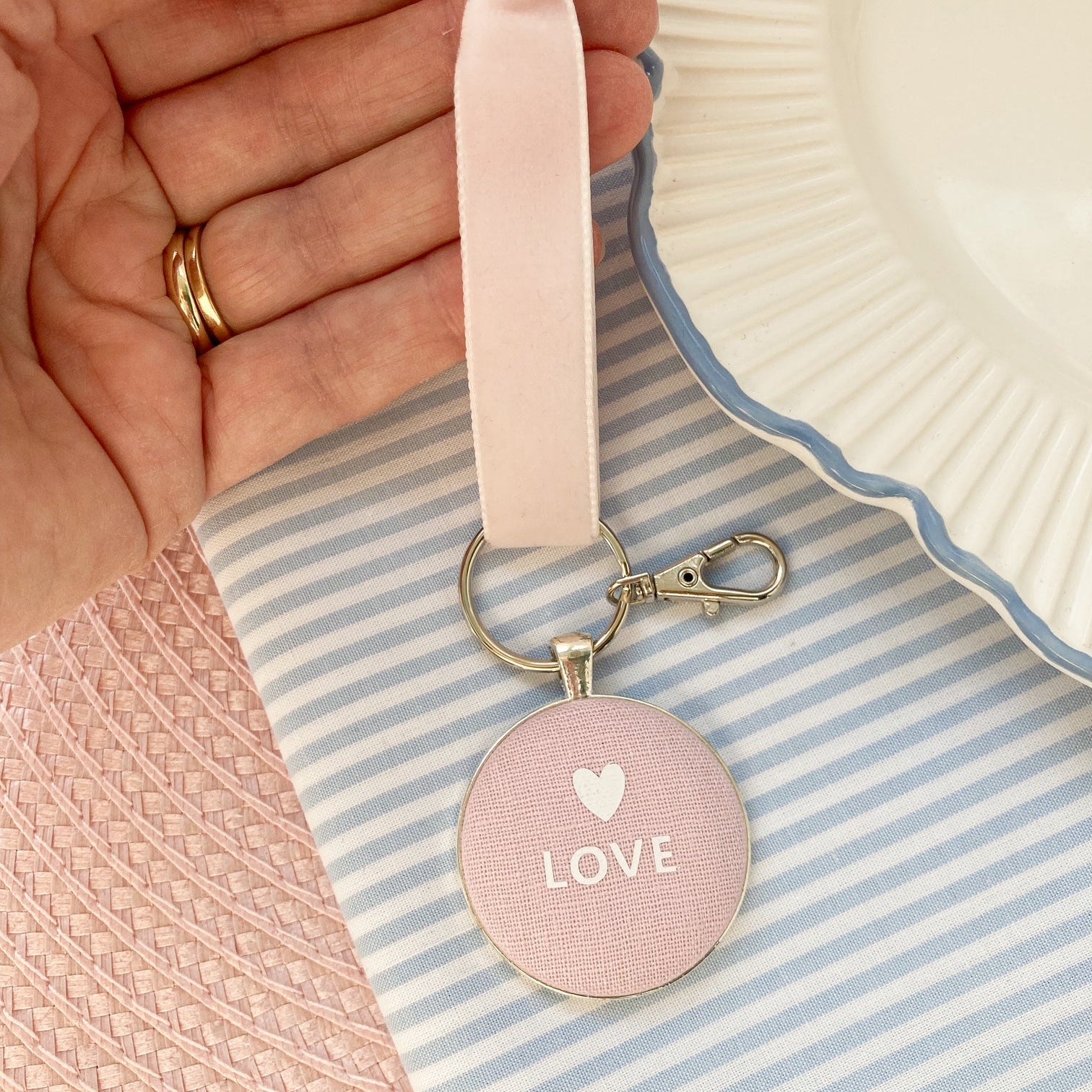 Pink keychain with 'LOVE' and heart symbol on pink linen fabric on a striped background