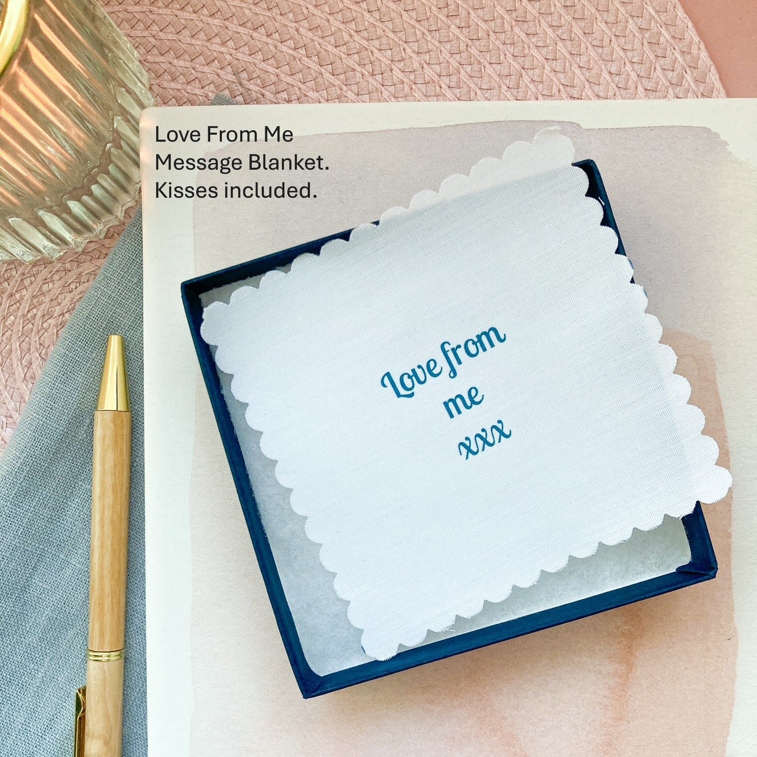 Message blanket with 'Love from me xxx' text, pen, and packaging on a pink textured surface.