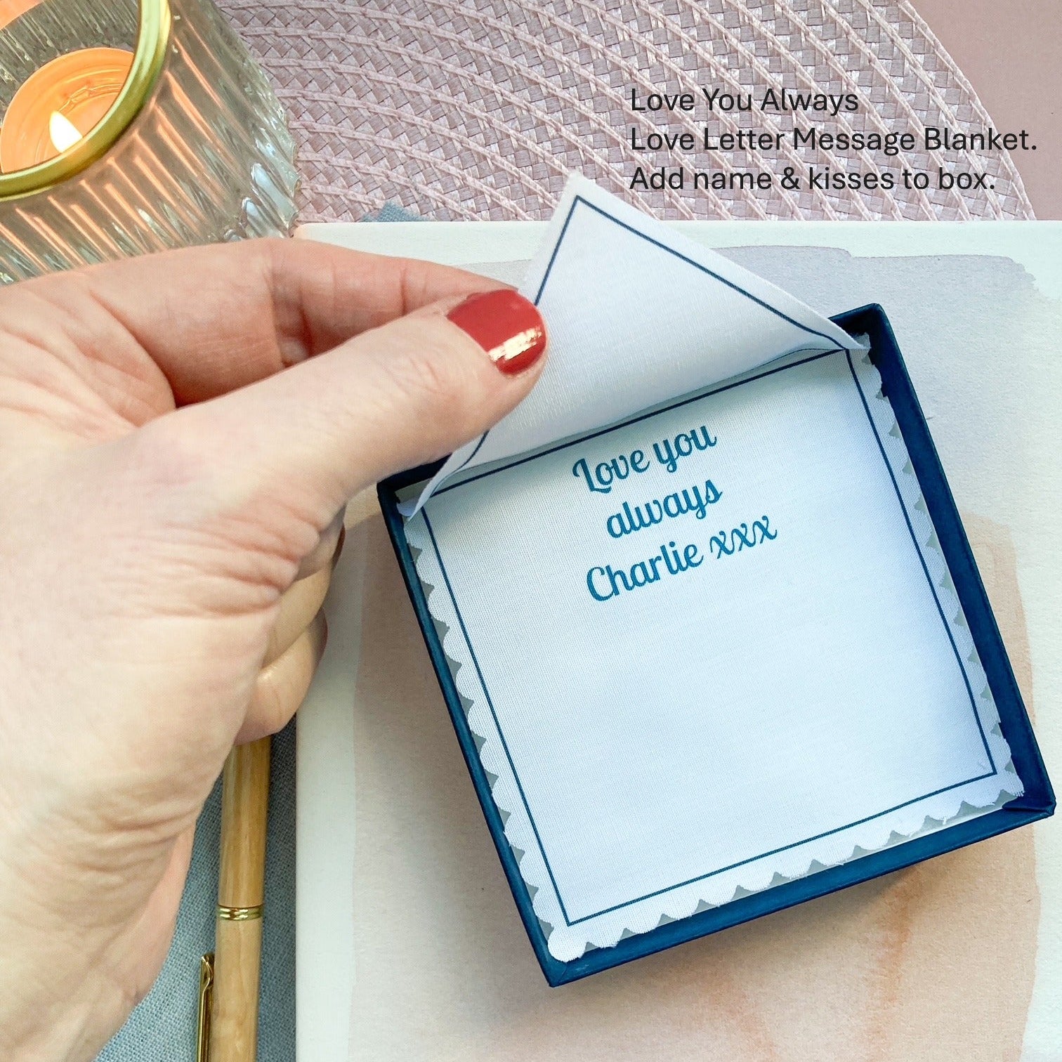 Hand holding a small box with 'Love you always' text, next to a journal on a textured surface.