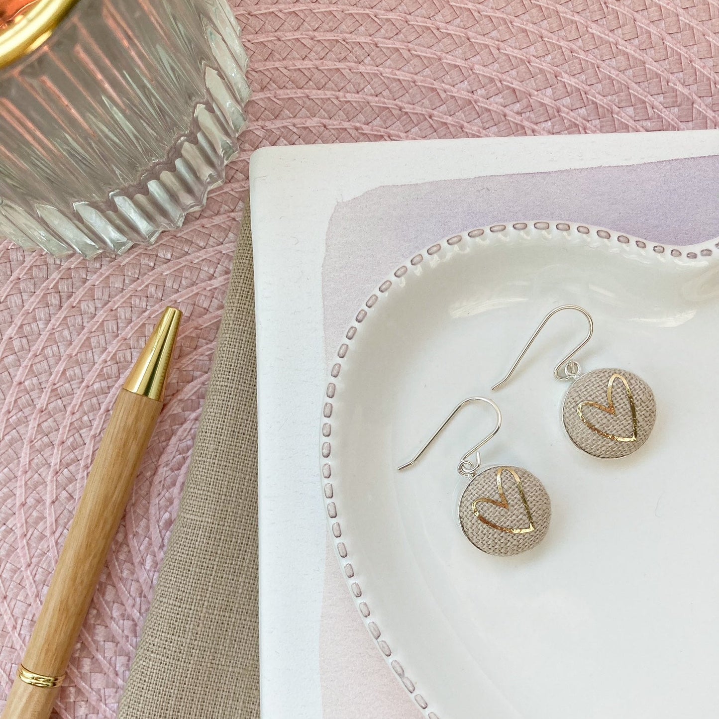 Gold & natural heart earrings on a white heart-shaped jewelry dish with a pink textured background