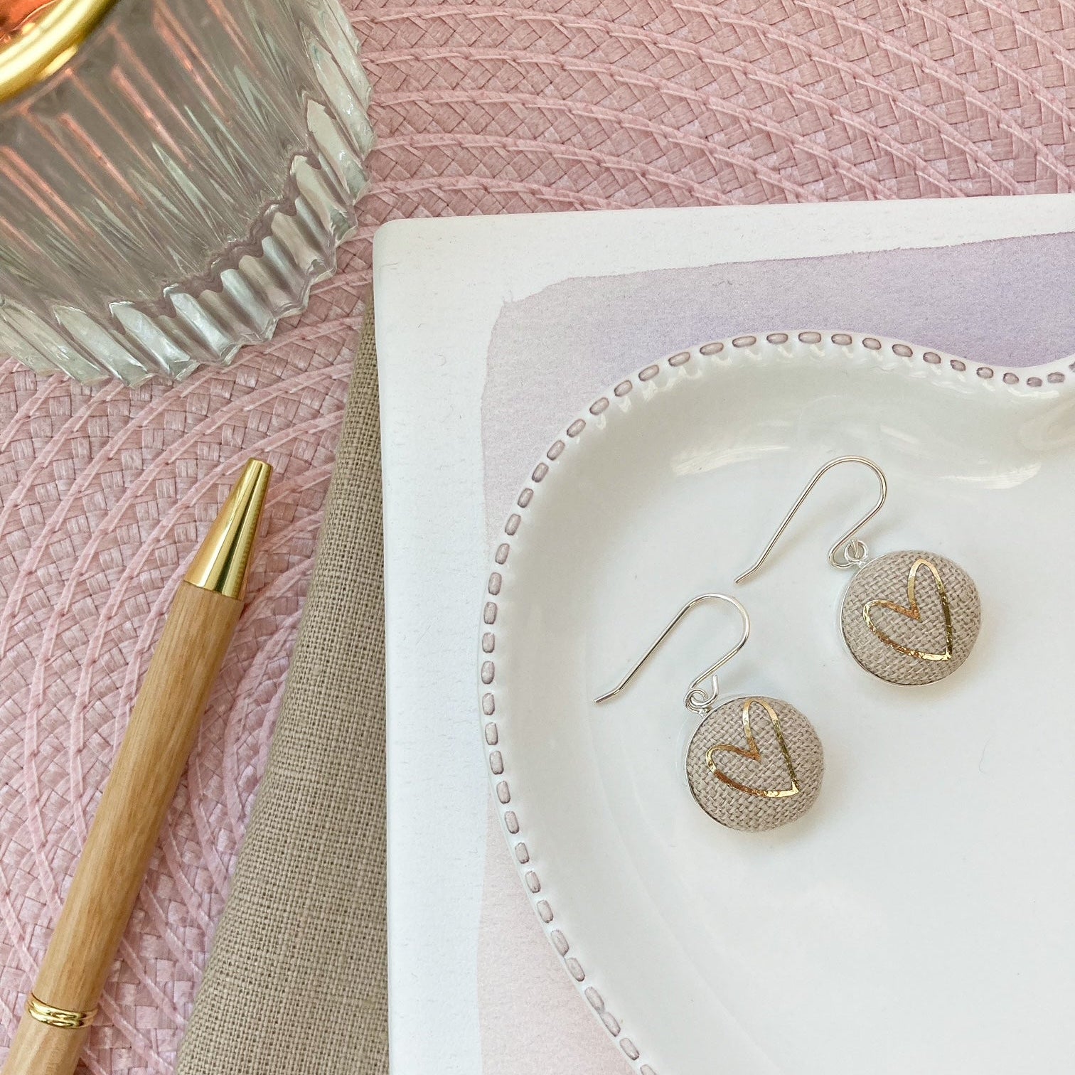 Gold & natural heart earrings on a white heart-shaped jewelry dish with a pink textured background