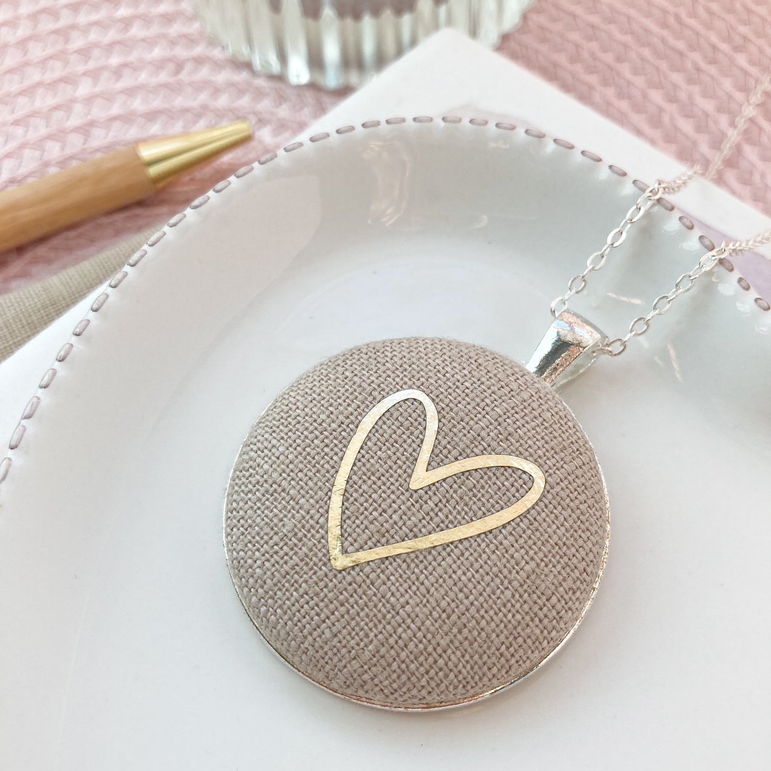 Necklace with a textured round pendant featuring a gold heart design on a white surface.