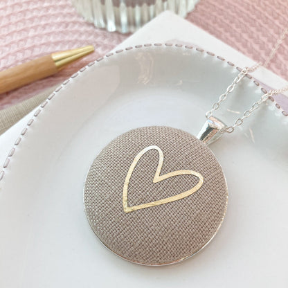 Necklace with a textured round pendant featuring a gold heart design on a white surface.