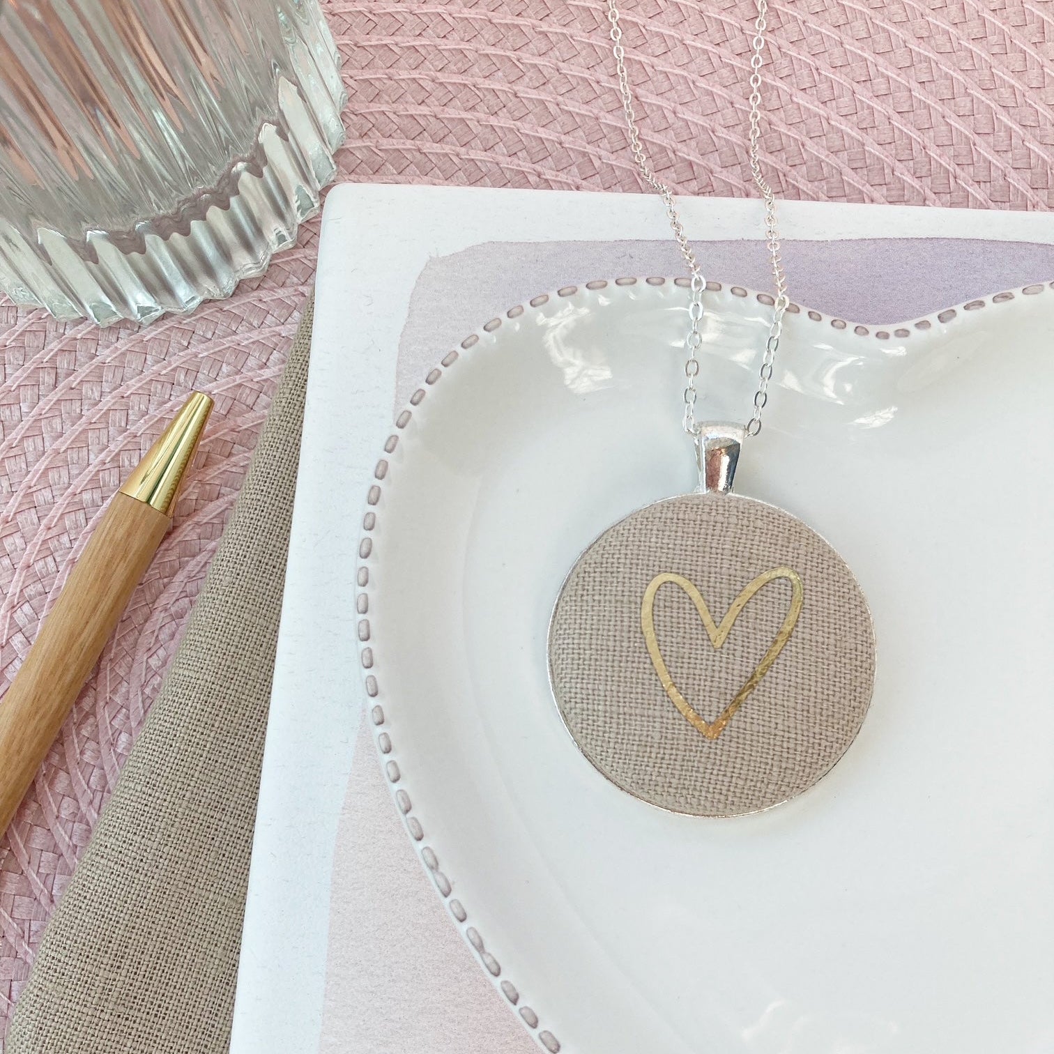 Necklace with heart pendant on a white card against a pink textured background