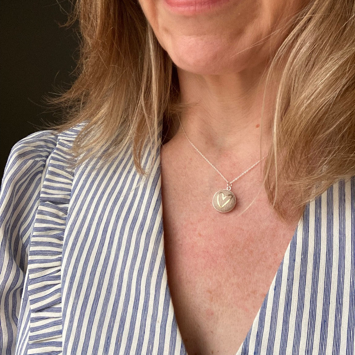 Woman wearing a natural and gold heart neckalce and a striped shirt