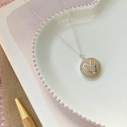 Necklace with a round pendant on a textured fabric surface with a pen.