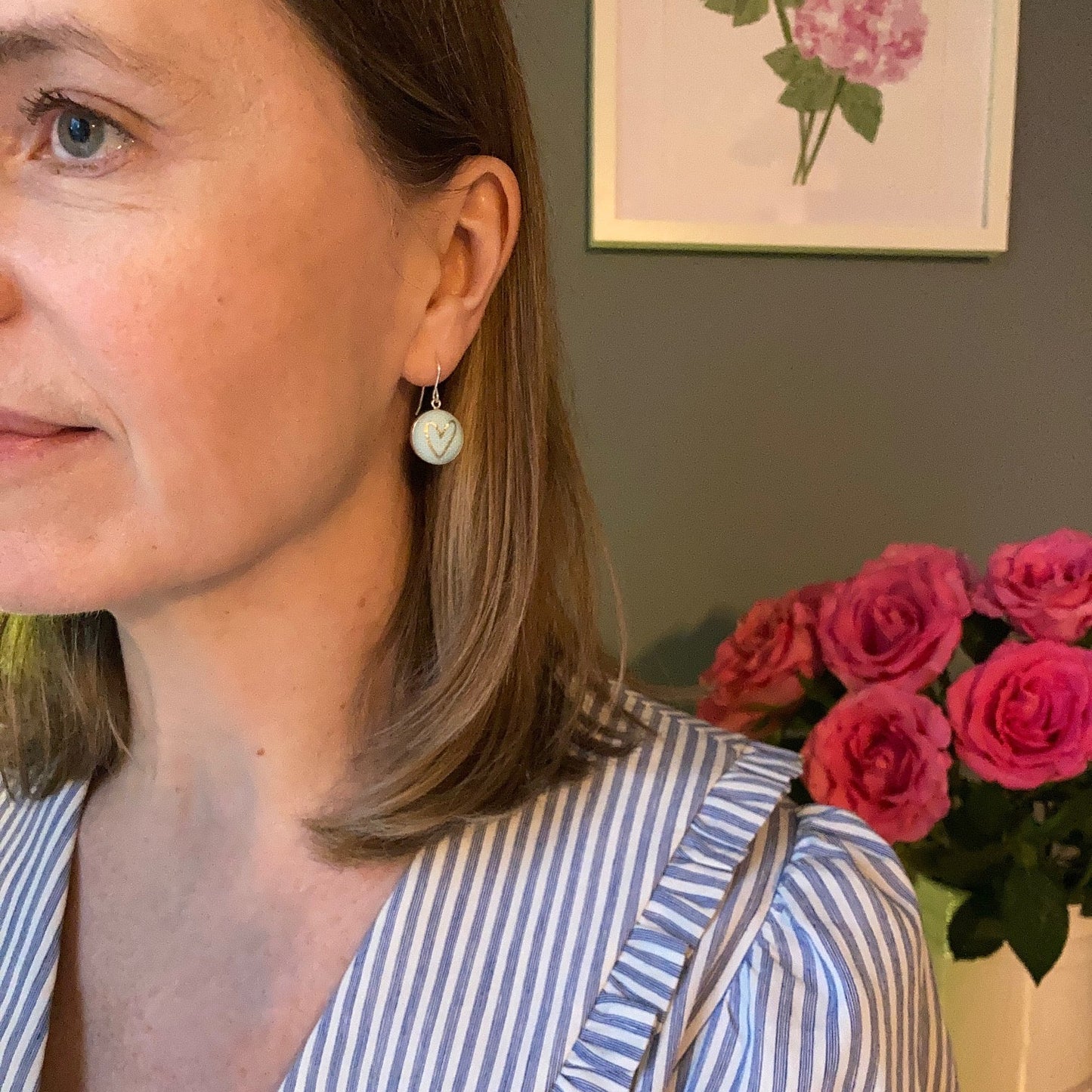 Close-up of a person wearing mint aqua heart earrings and a striped shirt featuring flowers in the background