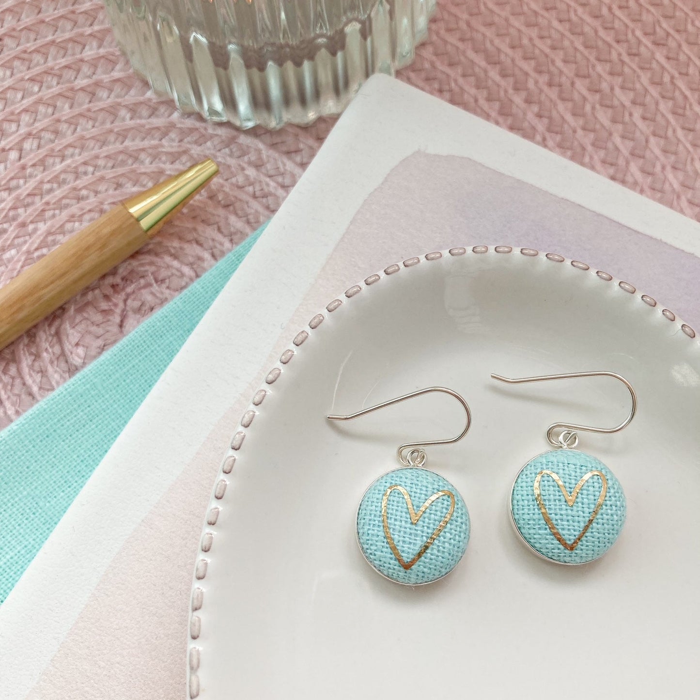 Pair of earrings with heart design on a white dish with a pink background