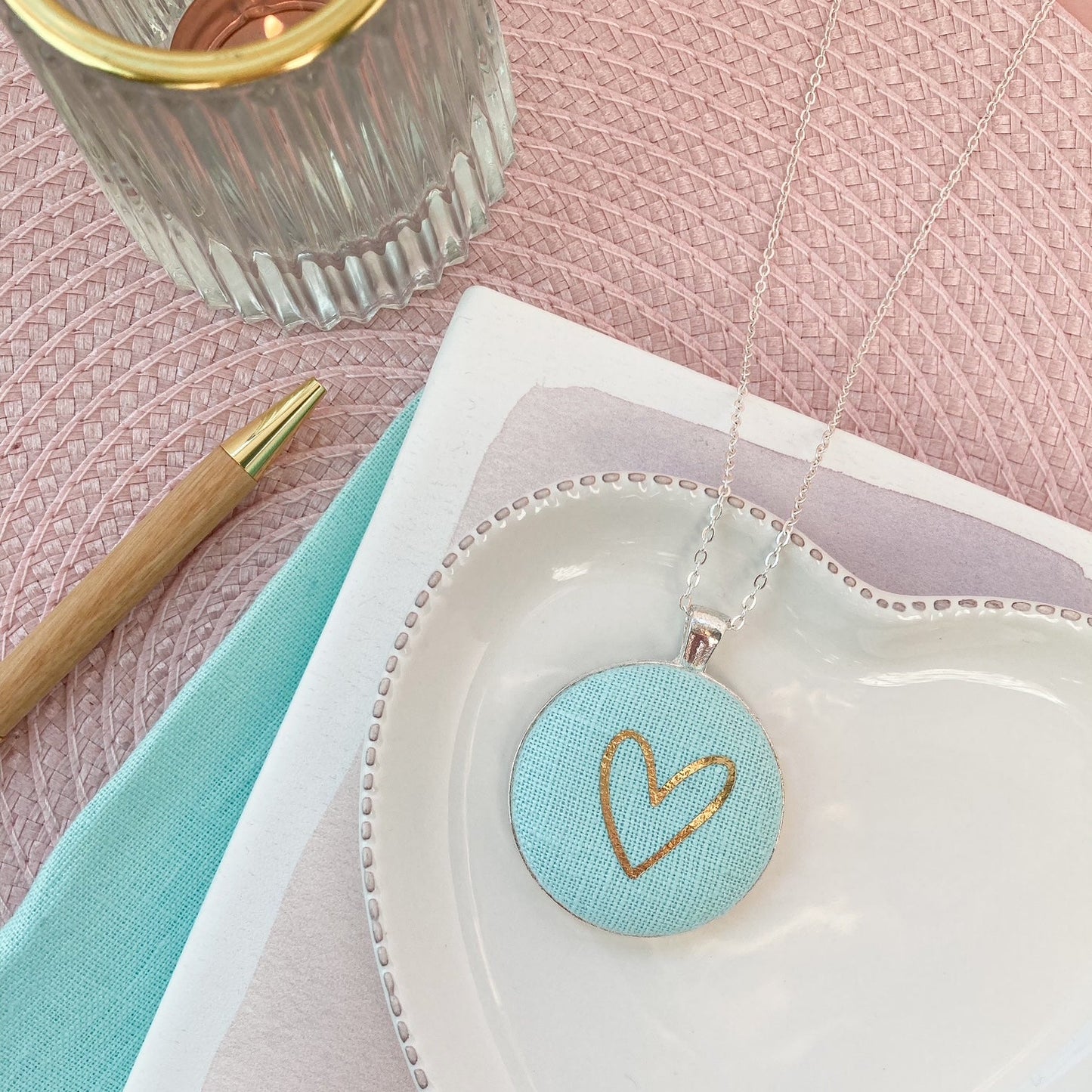 Jewelry dish with a heart-shaped pendant on a pink surface