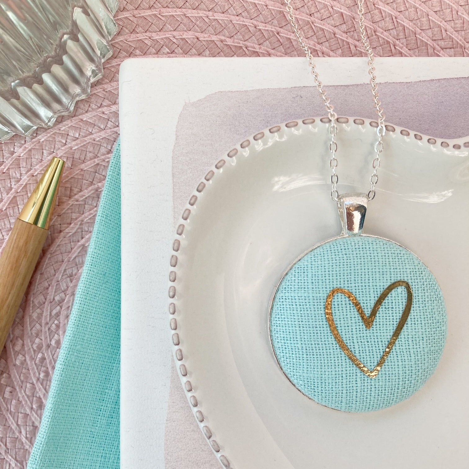 Necklace with a heart pendant on a white dish with a pink textured background