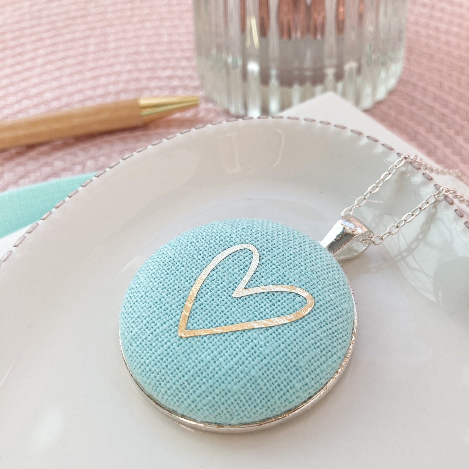 Light blue pendant with a gold heart design on a white dish.