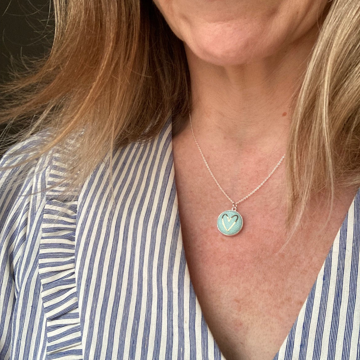 Woman wearing a mint aqua necklace with a heart design and a striped shirt