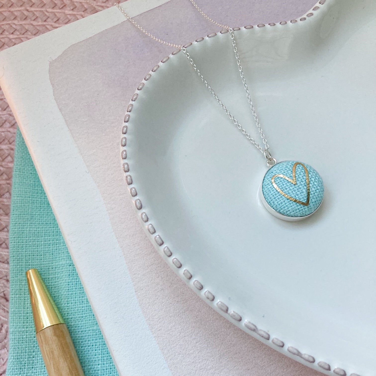 Necklace with a heart-shaped pendant on a textured surface with a pen.